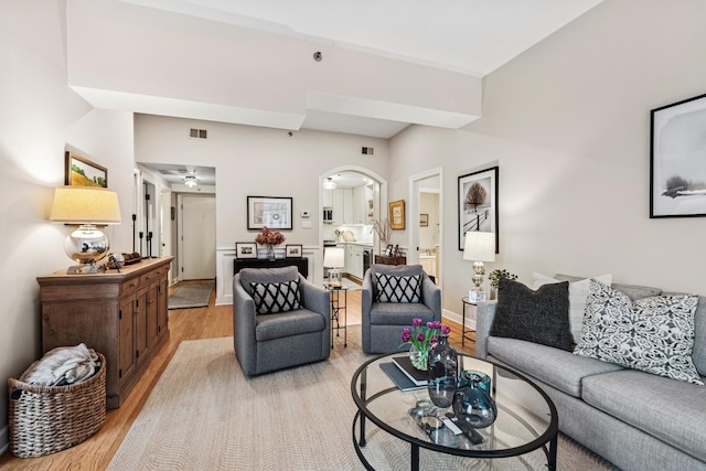living area featuring light wood finished floors, arched walkways, a ceiling fan, and baseboards