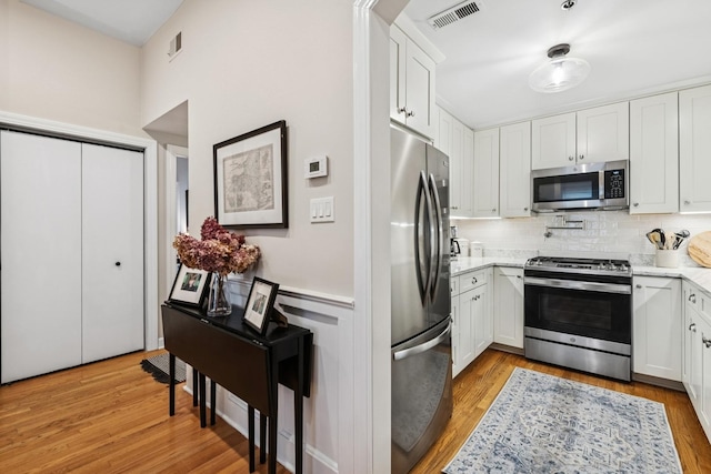 kitchen featuring appliances with stainless steel finishes, decorative backsplash, white cabinetry, light wood-style floors, and wainscoting
