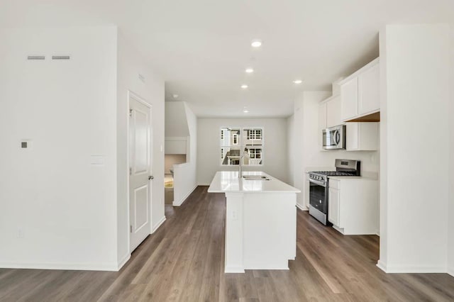 kitchen featuring an island with sink, white cabinets, appliances with stainless steel finishes, a sink, and wood finished floors