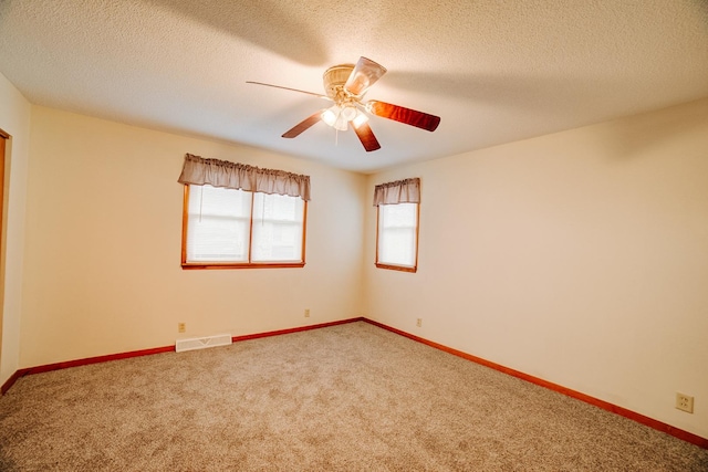 empty room with a textured ceiling, visible vents, baseboards, a ceiling fan, and carpet floors