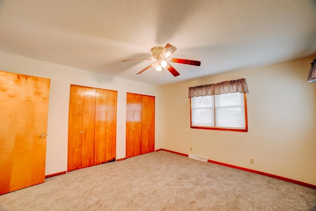 unfurnished bedroom with carpet flooring, baseboards, multiple closets, a textured ceiling, and visible vents