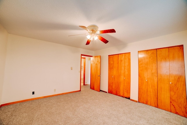 unfurnished bedroom featuring two closets, carpet, baseboards, a textured ceiling, and a ceiling fan
