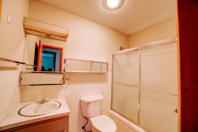 bathroom featuring shower / bath combination with glass door, toilet, vanity, a textured ceiling, and tile walls