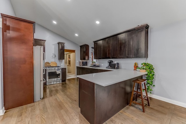 kitchen featuring vaulted ceiling, a peninsula, stainless steel appliances, light wood-style floors, and dark brown cabinets