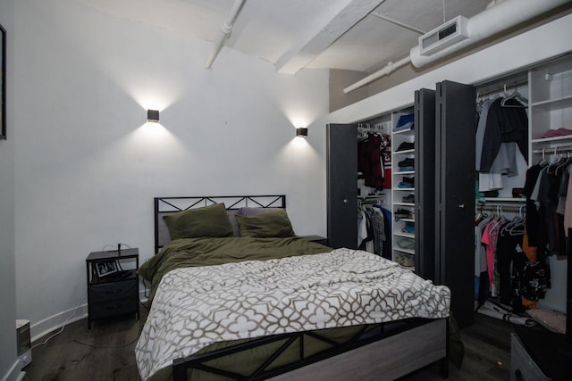 bedroom featuring beamed ceiling, two closets, and wood finished floors