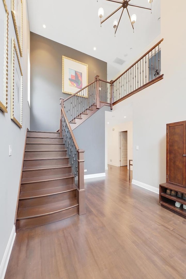 stairs with a towering ceiling, baseboards, an inviting chandelier, and wood finished floors