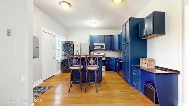 5110 S Woodlawn Ave Unit 2H, Chicago, IL 60615 - kitchen featuring light wood-style floors, blue cabinetry, a breakfast bar, appliances with stainless steel finishes, and stacked washer and clothes dryer