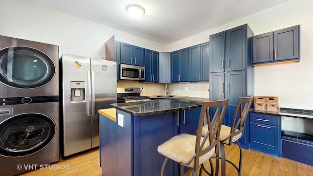 5110 S Woodlawn Ave Unit 2H, Chicago, IL 60615 - kitchen with a kitchen breakfast bar, blue cabinetry, stacked washing maching and dryer, appliances with stainless steel finishes, and light wood finished floors