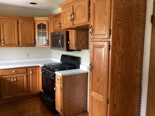 kitchen with light countertops, black gas range, brown cabinets, stainless steel microwave, and dark wood-type flooring