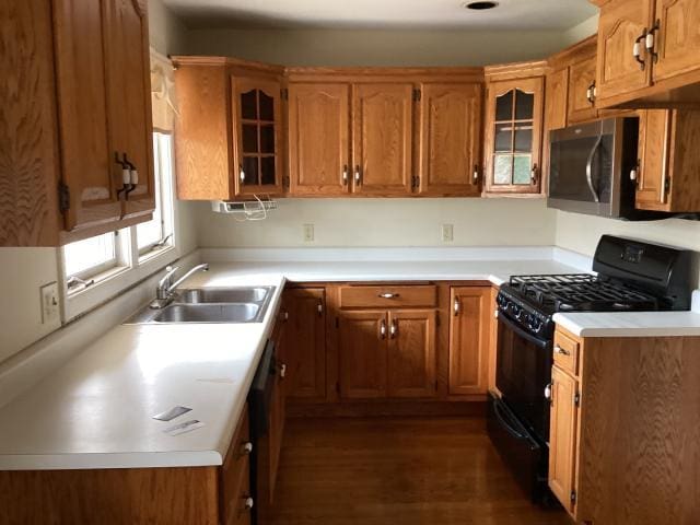kitchen with stainless steel microwave, a sink, brown cabinetry, and black gas range