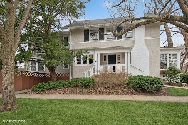view of front of home featuring a balcony, stucco siding, a front yard, fence, and covered porch