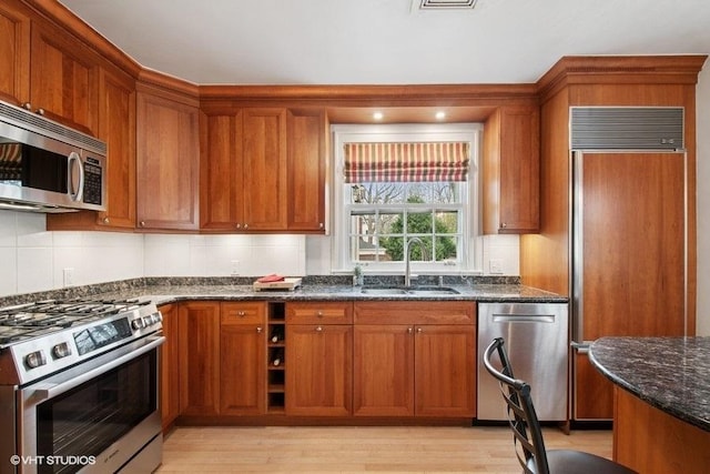 kitchen featuring brown cabinetry, dark stone counters, a sink, and stainless steel appliances