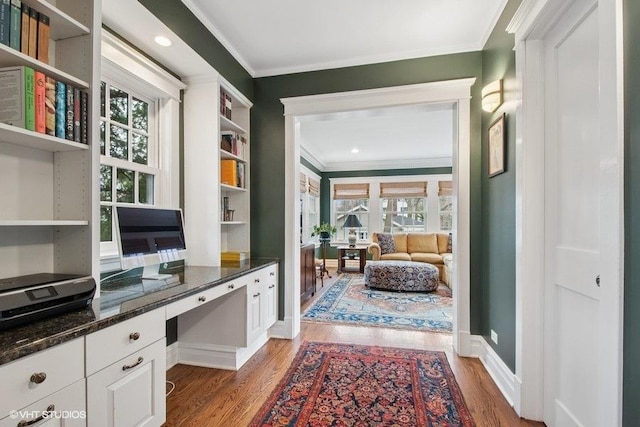 home office with crown molding, built in study area, baseboards, and light wood-style floors