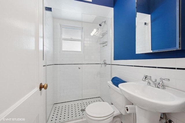 bathroom with a shower stall, tile walls, a sink, and toilet