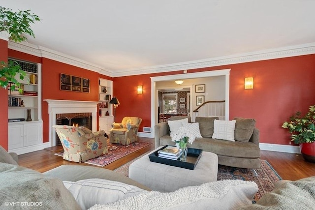 living area featuring a fireplace, baseboards, crown molding, and wood finished floors