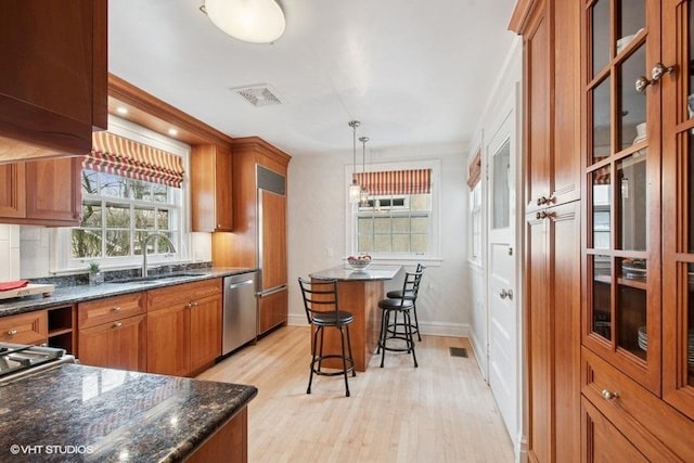 kitchen with a sink, light wood-type flooring, a breakfast bar, brown cabinets, and stainless steel dishwasher