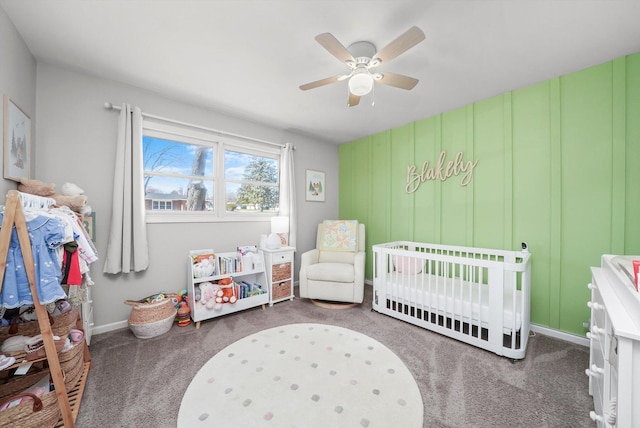 carpeted bedroom with a crib, baseboards, and a ceiling fan