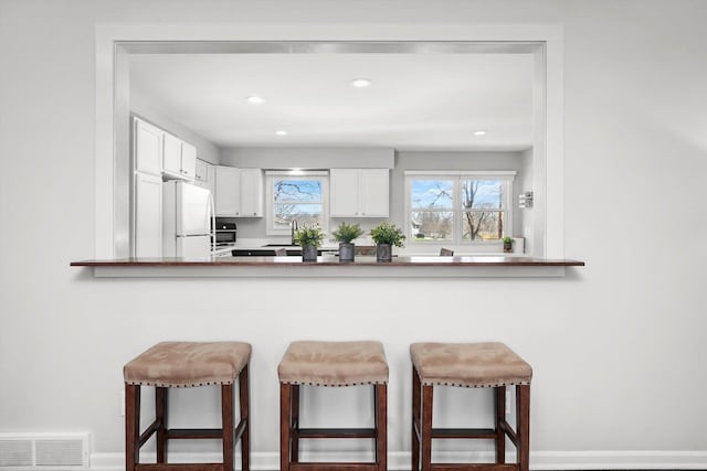 kitchen featuring a kitchen breakfast bar, a peninsula, freestanding refrigerator, white cabinets, and visible vents