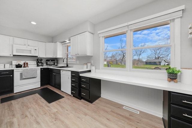 kitchen with white appliances, dark cabinets, white cabinets, visible vents, and a sink