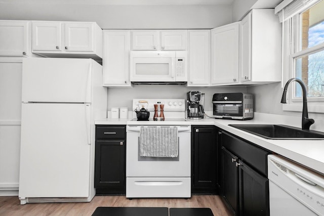 kitchen with white appliances, white cabinets, a sink, dark cabinetry, and light wood finished floors