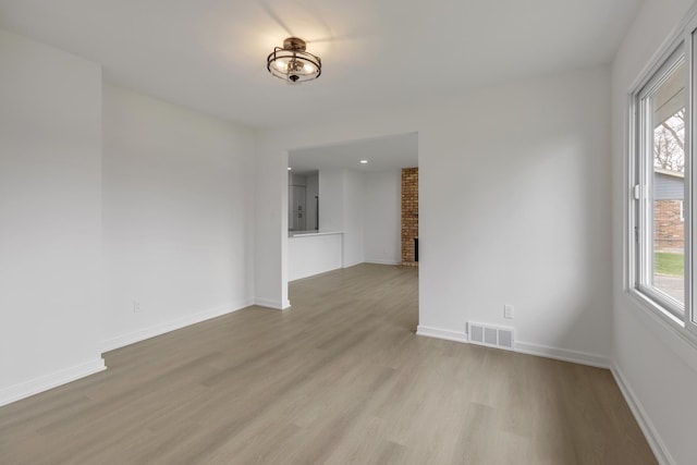 unfurnished room featuring light wood finished floors, baseboards, visible vents, and a brick fireplace