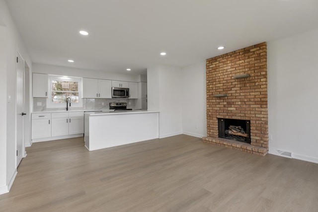 unfurnished living room with a sink, a brick fireplace, light wood-style flooring, visible vents, and recessed lighting