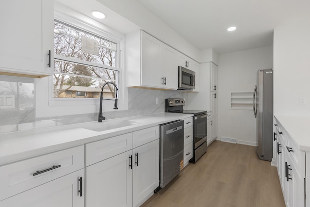 kitchen with a sink, tasteful backsplash, light wood-style flooring, stainless steel appliances, and white cabinets