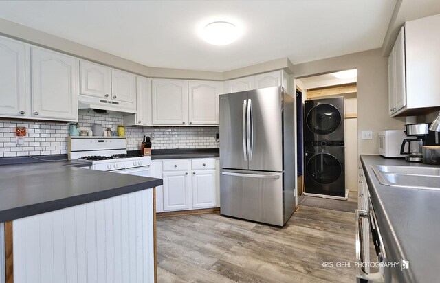 kitchen featuring freestanding refrigerator, white gas range oven, under cabinet range hood, dark countertops, and stacked washer / drying machine
