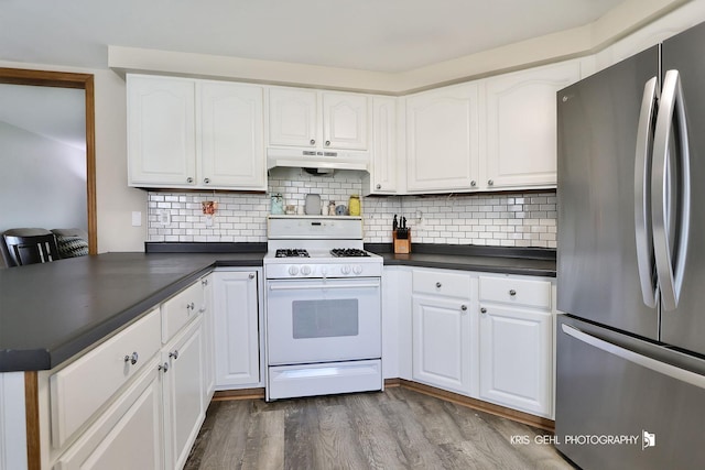 kitchen featuring dark wood-style flooring, dark countertops, freestanding refrigerator, under cabinet range hood, and white range with gas cooktop