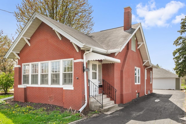 view of front of property with entry steps, a chimney, roof with shingles, brick siding, and a garage