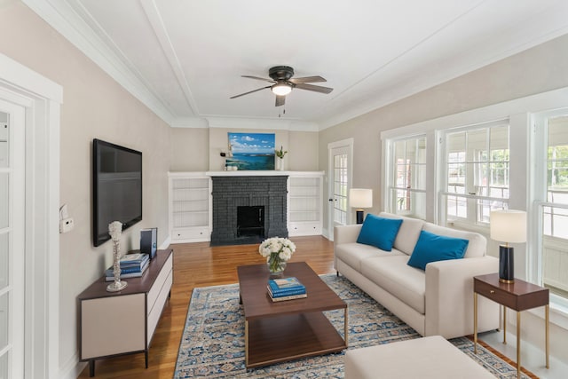 living room with wood finished floors, ornamental molding, ceiling fan, a fireplace, and baseboards