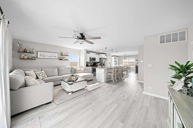 living room with visible vents, a ceiling fan, baseboards, and light wood-type flooring