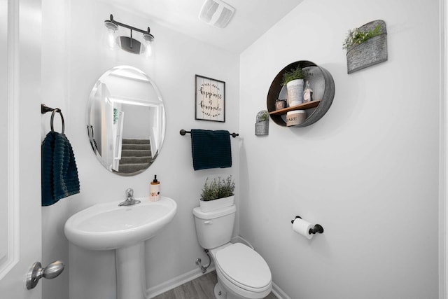 half bath with visible vents, baseboards, wood finished floors, and toilet