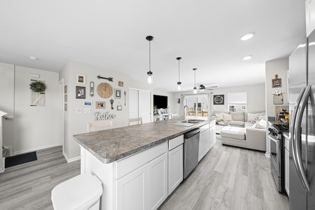 kitchen featuring ceiling fan, a sink, open floor plan, light wood-style floors, and stainless steel appliances