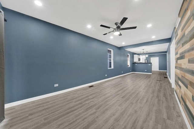 unfurnished living room with ceiling fan with notable chandelier, visible vents, recessed lighting, wood finished floors, and baseboards