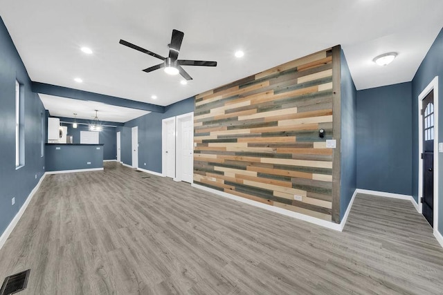 unfurnished living room featuring an accent wall, baseboards, visible vents, and wood finished floors