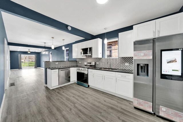 kitchen featuring dark countertops, appliances with stainless steel finishes, a peninsula, beam ceiling, and backsplash