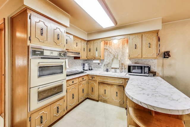 kitchen with tasteful backsplash, light countertops, under cabinet range hood, oven, and a sink