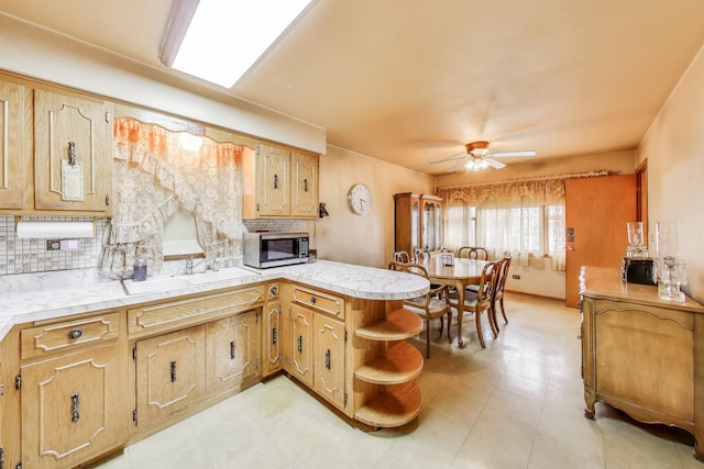 kitchen featuring a peninsula, stainless steel microwave, light countertops, a sink, and backsplash
