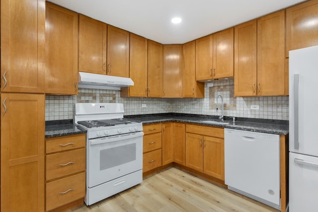 kitchen with white appliances, under cabinet range hood, a sink, light wood-style floors, and brown cabinetry