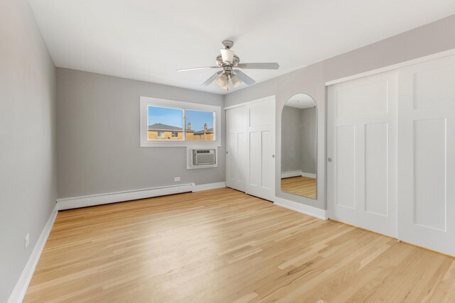 unfurnished bedroom featuring a wall unit AC, light wood-type flooring, baseboards, two closets, and a baseboard heating unit
