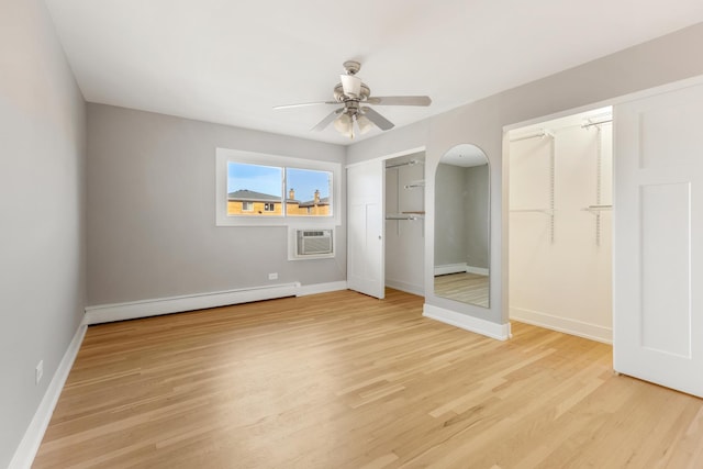 unfurnished bedroom with baseboards, a baseboard heating unit, an AC wall unit, and light wood-type flooring