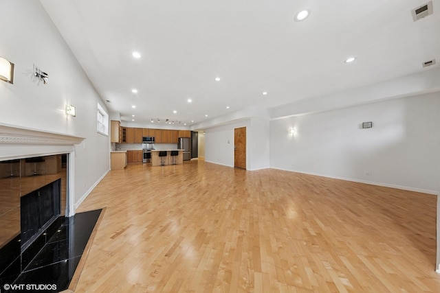 unfurnished living room featuring a fireplace with flush hearth, baseboards, visible vents, light wood-style floors, and recessed lighting