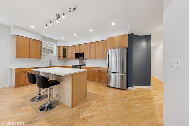 kitchen with light countertops, a breakfast bar area, stainless steel appliances, a kitchen island, and a sink