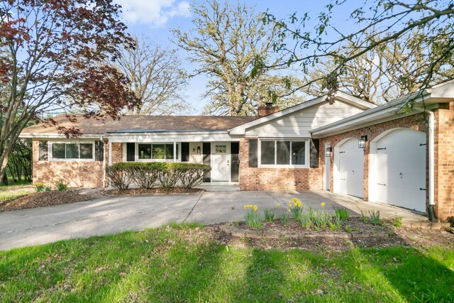 ranch-style home with an attached garage, a chimney, driveway, and brick siding