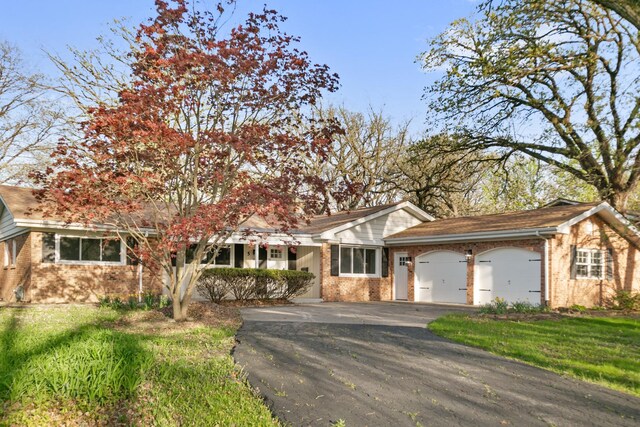 ranch-style house featuring brick siding, a garage, aphalt driveway, and a front yard