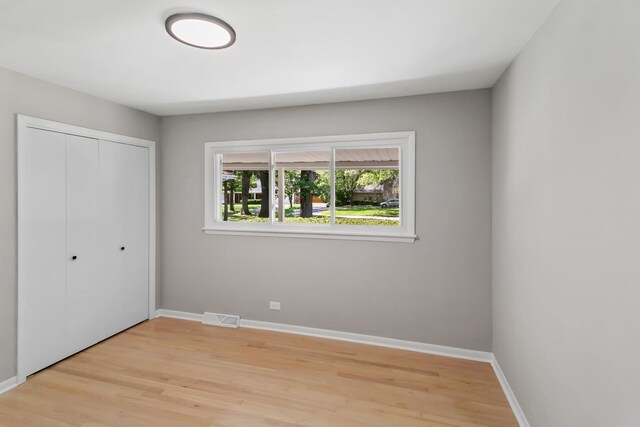 unfurnished bedroom with a closet, baseboards, visible vents, and light wood-style floors