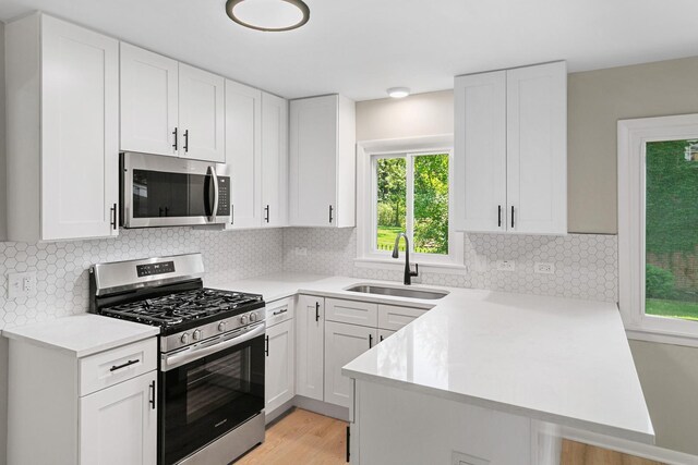 kitchen featuring white cabinets, a sink, light countertops, stainless steel appliances, and a peninsula