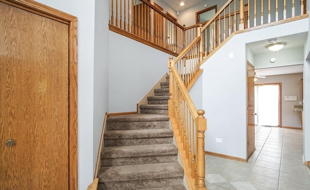 staircase featuring baseboards, tile patterned flooring, a high ceiling, and recessed lighting