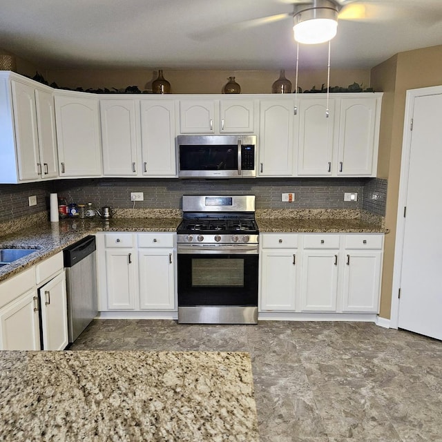 kitchen featuring appliances with stainless steel finishes, white cabinetry, dark stone countertops, and backsplash